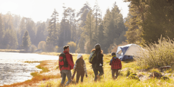 family of 4 hiking back to their tent at a campsite along the river