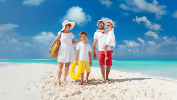 Happy family on vacation in colourful clothing on walking down a white sand beach with clear blue skys in the background