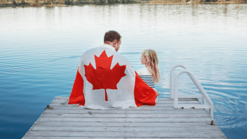 Father and Daughter sitting on a lake dock in summer with Canadian flag wrapped around them