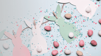 Paper craft of tri-colour easter bunnies with cotton ball tails and egg shaped candy and confetti sprinkled around  