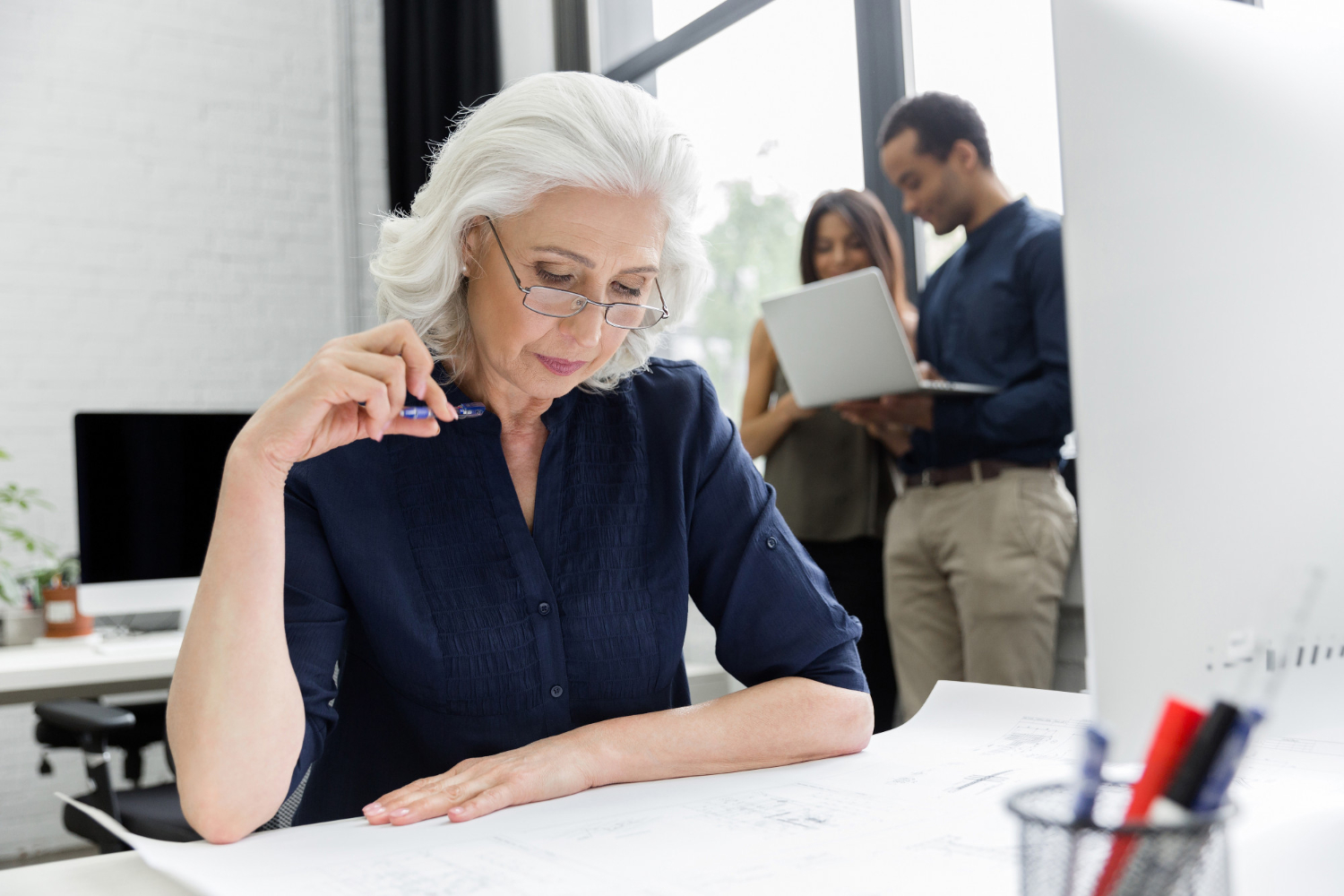 white haired woman reviewing work at her desk