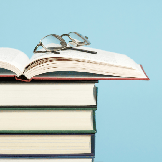 a stack of books with an open book on top and glasses sitting on the open book