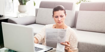 woman sitting on the floor in front of a couch with her laptop and some paperwork that she is looking at