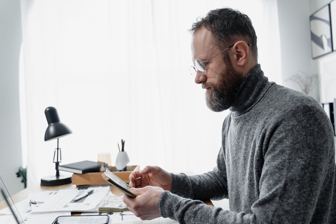 man in grey sweater counting money at office