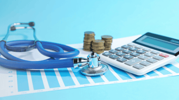 Stethoscope on a table with stacked coins, a calculator and a health chart