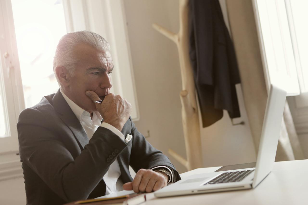 white haired man looking pensively at a laptop