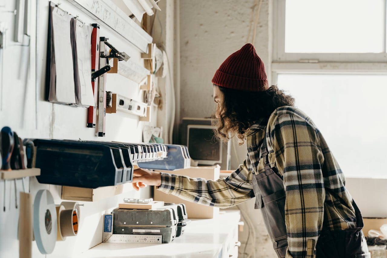 person with long hair and a beaning picking something up off a work bench