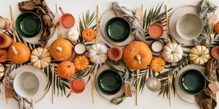 thanksgiving table setting with cups, bowls, pumpkins and greenery