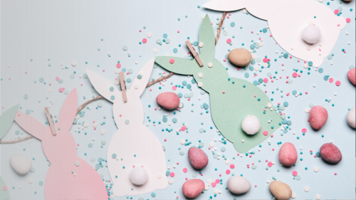 Paper craft of tri-colour easter bunnies with cotton ball tails and egg shaped candy and confetti sprinkled around  