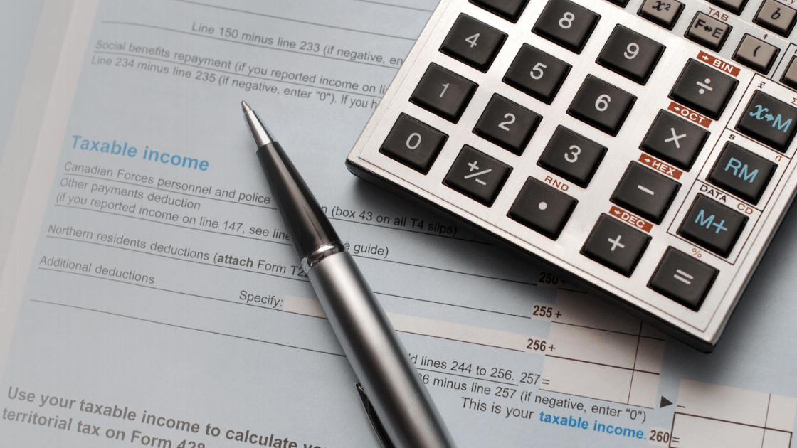 Close-up of a tax form with instructions for calculating taxable income, a pen resting on the form, and a calculator placed on top of the pen.